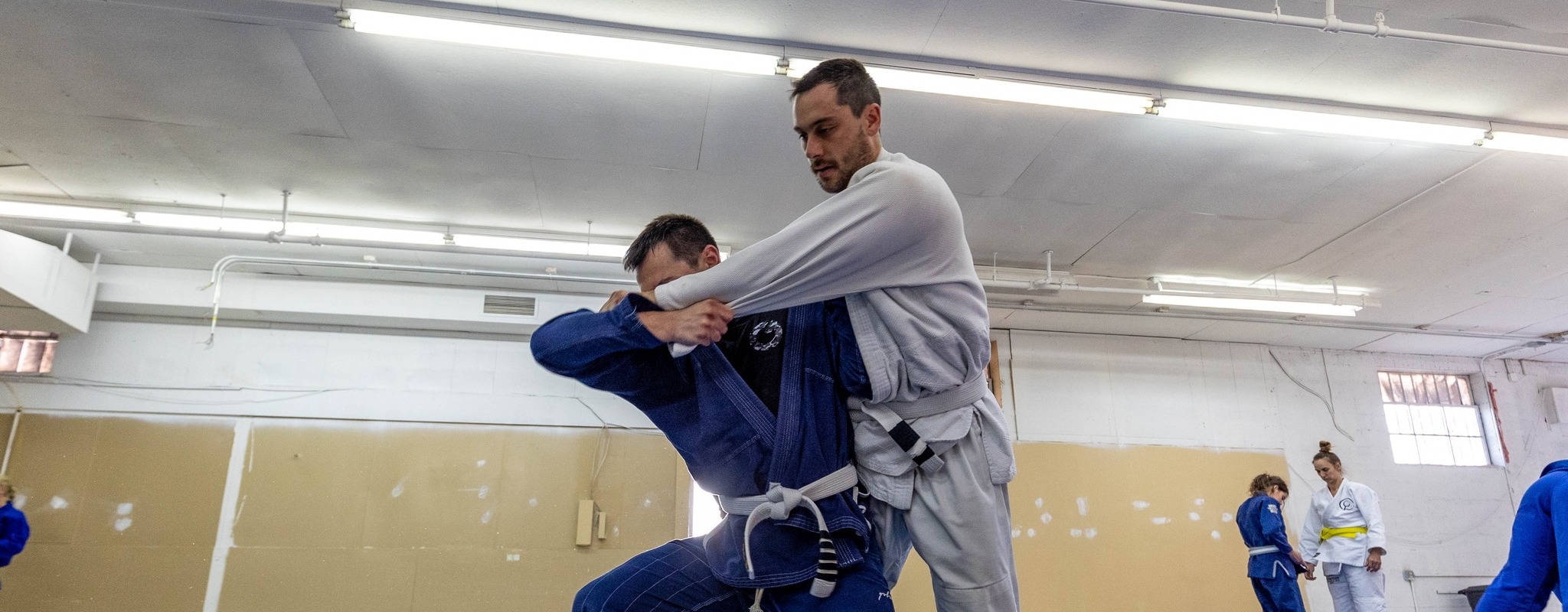BJJ student practice on the mats, with one student about to be thrown over the shoulder of another