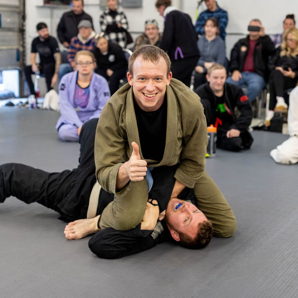 a smiling student gives a thumb's up as he pins his partner in BJJ class